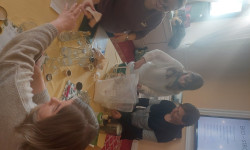 Cztery kobiety przy stole. Dwie siedzą dwie stoją i mieszają łyżkąprodukty w wiaderku. 