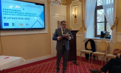 Konferencja LGD. Hrubieszów. W sali mężczyzna przemawia do zebranych osób. Za nim ekran z prezentacją. 