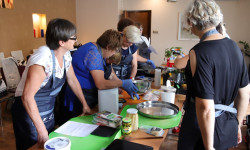 w sali przy długim stole kilka kobiet stoi na stole naczynia kuchenne kobiety gotują 