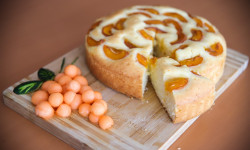 na desce okrągłe ciasto z jednym wyciętym kawałkiem obok kulki z melona 