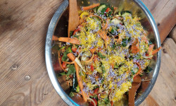 na drewnianym stole metalowa, okrągła miska z sałatką z cukinii, marchewki, ogórka udekorowana kwiatami mniszka lekarskiego