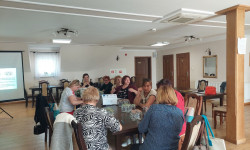 w  sali przy długim stole grupa ludzi słucha wykłady 