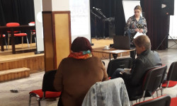 grupa ludzi przy stole i osoba prowadząca rozmawiają