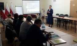 grupa ludzi przy stole i osoba prowadząca rozmawiają