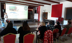 grupa ludzi przy stole i osoba prowadząca rozmawiają