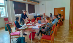 grupa uczestników spotkania siedzących przy stole słuchają wypowiedzi osoby prowadzącej