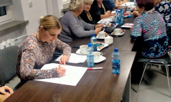 siedzący przy stole uczestnicy spotkania wykonują zadania w grupach zlecone przez prowadzącego spotkanie