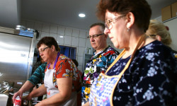 dwie kobiety i mężczyzna przy blacie kuchennym przyrządzają potrawę