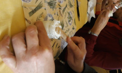 Dłonie oparte o brzeg stołu mieszają szpatułką w małym słoiku biały proszek.