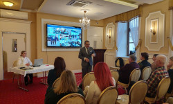 Konferencja LGD. Hrubieszów. W sali mężczyzna przemawia do zebranych osób. Za nim ekran z prezentacją.