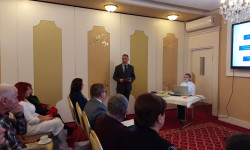 Konferencja LGD. Hrubieszów. W sali mężczyzna przemawia do zebranych osób. Za nim ekran z prezentacją.