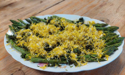 na drewnianym stole na białym owalnym talerzu  smażone szparagi polane ziołowym pesto udekorowane kwiatem mniszka lekarskiego 