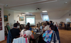 w  sali przy długim stole grupa ludzi słucha wykłady 