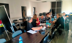 grupa uczestników spotkania siedzących przy stole słuchają wypowiedzi osoby prowadzącej